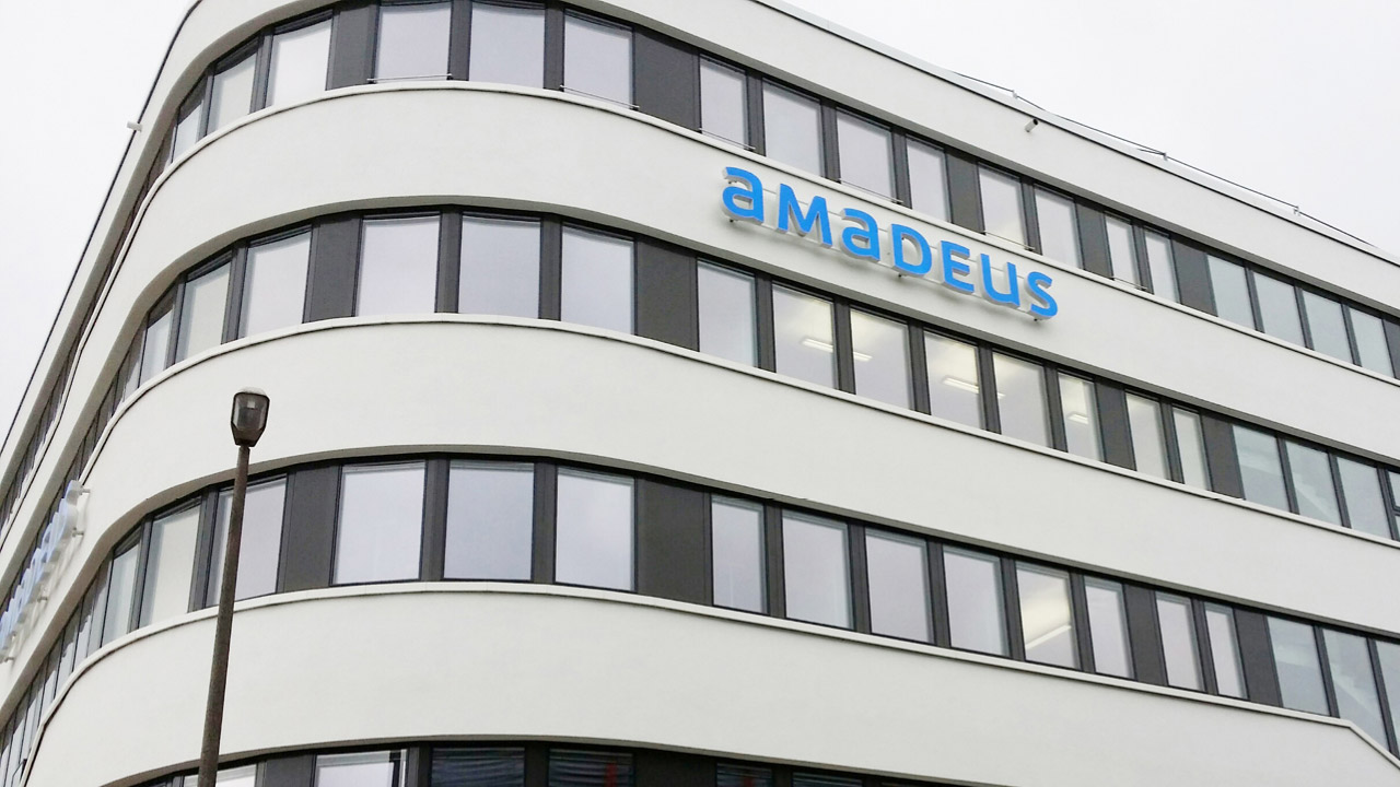 Leuchtschrift „Amadeus“ an der Fassade eines modernen Bürogebäudes mit abgerundeten Ecken.