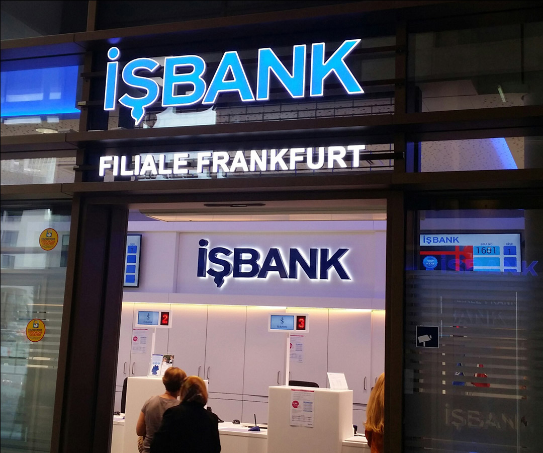 Eingang einer IŞBANK-Filiale in Frankfurt mit beleuchtetem Schild über der Tür bei Nacht.